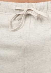 I pantaloni della tuta grigi chiari presentano una texture morbida, una vita elasticizzata e un cordoncino per la regolazione. Dettaglio delle cuciture visibile lungo il lato.