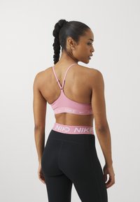 Sostén deportivo de color rosa claro con tirantes ajustables y una banda con marca, combinado con leggings negros de cintura alta que presentan una cinturilla rosa a juego.