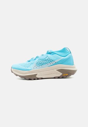 Lyseblå sportsko med mesh-overdel, beige tykk såle, Vibram-logo på yttersålen og lisser, vist fra innsiden.