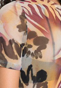 Transparent, lätt tyg med ett färgglatt abstrakt mönster som har bruna, orange och gula toner. Korta ärmar med en åtsittande design.
