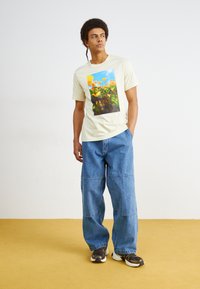 Tricou galben deschis cu imprimeu floral colorat; blugi din denim albastru deschis, largi; adidași negri și albi.