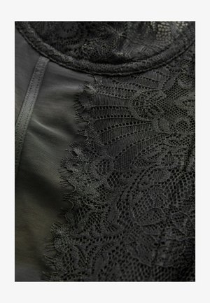 Juodas nėrinių audinys ant lygaus juodo paviršiaus, turintis sudėtingus gėlių raštus, tekstūruotus kraštus ir švelnų blizgesį.