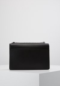 Borsa a tracolla nera in pelle, di forma rettangolare, con superficie testurizzata, tracolla in catena argentata e design minimalista. Dotata di chiusura magnetica piatta.