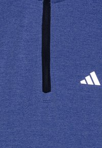 Primo piano di un tessuto blu con una cerniera nera e il logo Adidas bianco sul lato destro.