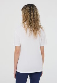 T-shirt bianco in cotone con maniche corte, vestibilità rilassata e orlo leggermente arrotondato. La vista posteriore mostra una texture liscia e senza marchi visibili.
