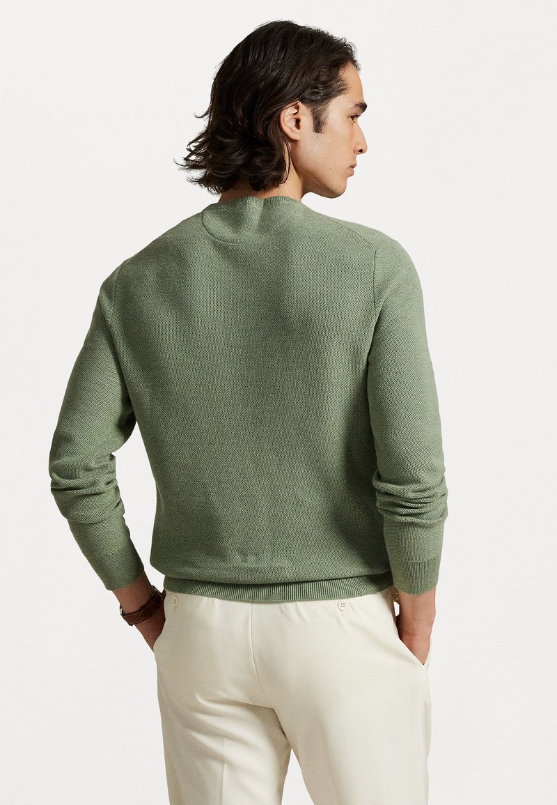Grüner gestrickter Pullover mit strukturiertem Finish, geripptem Saum und Bündchen, rundem Halsausschnitt und tailliertem Design. Getragen mit hellen Hosen.