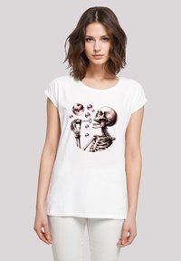 Weißes Baumwoll-T-Shirt mit einem grafischen Design eines Skeletts, das rosa Blasen, einschließlich einer herzförmigen Blase, blasst. Entspannte Passform, umgeschlagene Ärmel.