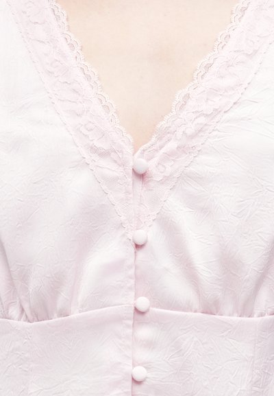 Ανοιχτό ροζ μπλούζα από ύφασμα με V-λαιμόκοψη διακοσμημένη με δαντέλα, τέσσερα κουμπιά μπροστά και υφασμένο λουλουδάτο σχέδιο.