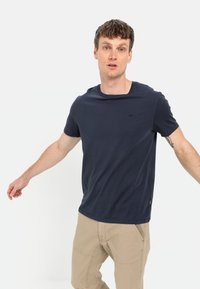 Marineblå bomulds t-shirt med rund halsudskæring, korte ærmer og et diskret logo på brystet. Båret sammen med beige bukser.