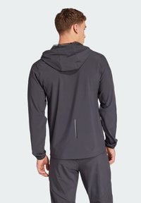 Waterdichte donkergrijze jas met een capuchon, strak ontwerp, lange mouwen en een discrete achterzak. Glad textuur en minimale details.