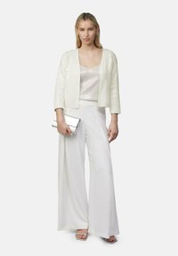 Weißer Paillettenjacke, silbernes Cami-Oberteil und weiße weite Hose. Eine silberne Clutch und Riemchensandaletten runden den Look ab.
