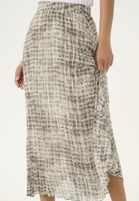 Falda midi plisada en beige claro con patrón abstracto gris, que cuenta con una cinturilla elástica y aberturas laterales para facilitar el movimiento.