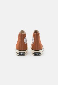 Sneakers arancioni alta con tomaia in tela, suole in gomma, cuciture bianche e patch circolari con logo sui lati esterni, caratterizzati da accenti neri a contrasto.
