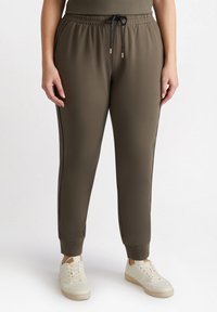 Khaki joggers med elastisk midjeband, dragsko, sidostrick, smalnade ben och ribbad mudd, i kombination med vita sneakers.