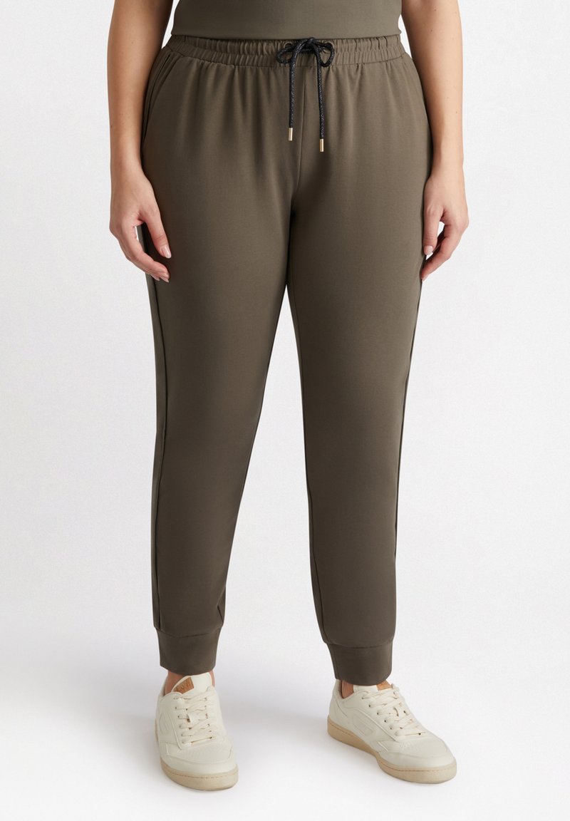 Khaki joggers med elastisk midjeband, dragsko, sidostrick, smalnade ben och ribbad mudd, i kombination med vita sneakers.