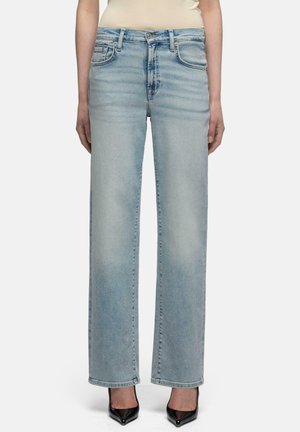 Osoba ma na sobie jasnoniebieskie jeansy o prostych nogawkach i czarne buty na wysokim obcasie z zaostrzonym przodem, stoi na jednolitym białym tle.