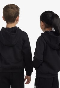 Fekete kapucnis pulóverek, puha anyagból készültek, bordázott mandzsettákkal és derékrésszel, hátulról látható két gyermek viseli őket.