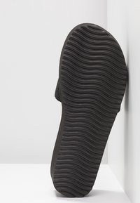 Semelle de chaussure en caoutchouc noir avec un motif texturé et rainuré, présentant un bord lisse et arrondi ainsi qu'une légère courbe au talon.