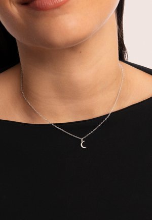 Silberne Halskette mit einem kleinen Halbmonden-Anhänger, verziert mit funkelnden Details, getragen über einem dunklen Oberteil.