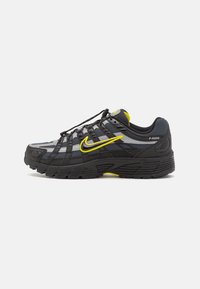Black and gray athletic shoes with a mesh upper, featuring a prominent yellow Nike swoosh, webbed lacing, and textured rubber outsole.
