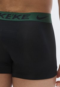 Sorte boxer briefs med en tætsiddende pasform og et grønt elastikbånd med Nike-branding. Glat tekstur uden synlige mønstre eller hardware.