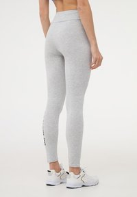 Leggings grigi alti in vita realizzati in tessuto testurizzato, con una vestibilità aderente e un dettaglio del logo nero lungo il lato, abbinati a sneaker bianche.