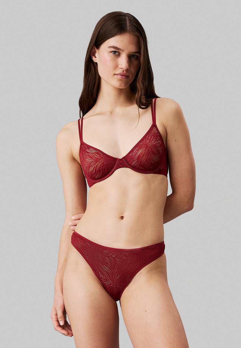 Set di lingerie in pizzo bordeaux composto da un reggiseno leggermente imbottito con spalline regolabili e un abbinato perizoma a vita alta, che mostra intricate fantasie floreali.
