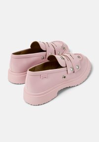 Zapatillas rosa tipo slip-on con correas decorativas y botones metálicos, que cuentan con una suela resistente y un diseño casual.