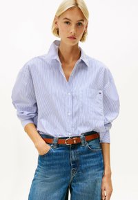 Blauw en wit gestreepte button-up shirt met een kraag, voorzien van lange mouwen en een borstzak, gecombineerd met hoge blauwe jeans en een bruine riem.