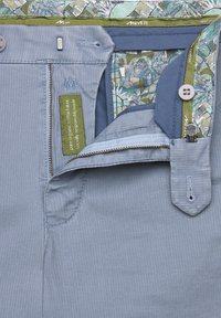 Light blue organic cotton pants feature a zip fly, button closure, and interior patterned lining with green accent details.
