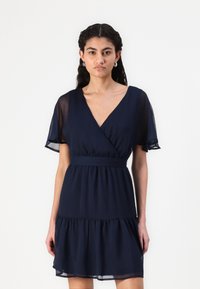 Ναυτικό μπλε φόρεμα τύπου wrap από ελαφρύ ύφασμα, με κοντά φτερωτά μανίκια, εφαρμοστή μέση και φουσκωτό στρίφωμα.