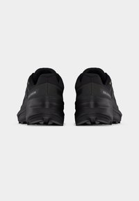 Ζεύγος μαύρων παπουτσιών trail running της Salomon, εμφανιζόμενα από πίσω, με παχιές σόλες και εμφανές πέλμα σε λευκό φόντο.