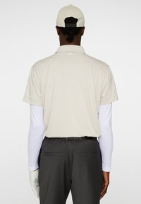 Beige pikétröja med kort krage, bärs över en vit långärmad topp, i kombination med mörkgrå byxor. Kepa i en matchande beige nyans.