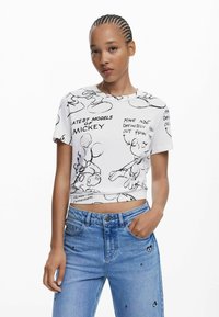 Tricou scurt alb, cu desene în negru cu Mickey Mouse și text, mâneci scurte, gât rotund, asortat cu blugi albaștri deschiși.