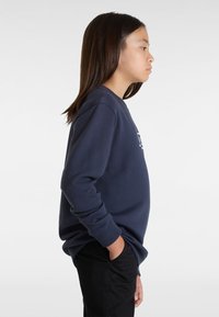 Felpa blu navy con maniche lunghe, scollo a girocollo e logo frontale. Abbinata a pantaloni neri, vista di lato. Texture liscia.