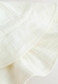 Tissu couleur crème avec une surface douce et texturée, présentant de subtils motifs froissés et des bords soigneusement cousus.