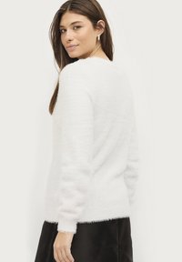 Witte fuzzy trui met een ronde hals, lange mouwen en geribbelde boorden. Zachte textuur en een licht losse pasvorm, gestyled met een donkere rok.