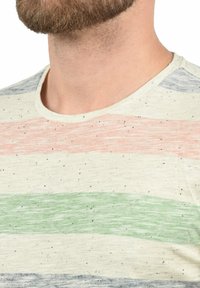 Bavlněné tričko s kulatým výstřihem, které má vodorovné pruhy v korálové, zelené a modré barvě na světle krémovém pozadí s tečkami.