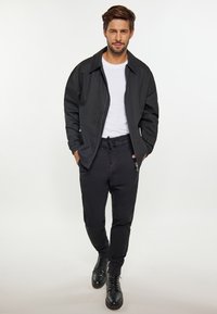 Jachetă bomber neagră, tricou alb și pantaloni negri. Jacheta are guler și fermoar, iar pantalonii au șnur și buzunare laterale. Botine negre.