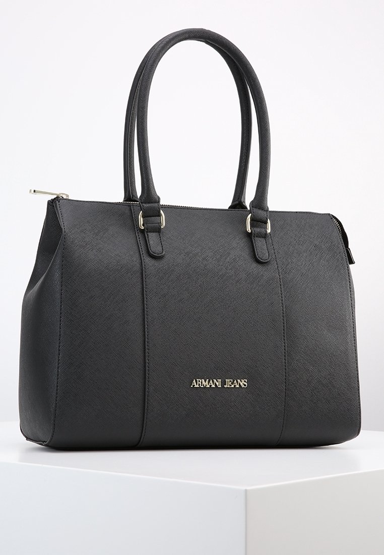 Czarna torebka skórzana o fakturze, z dwoma uchwytami i złotym logo Armani Jeans na przodzie, umieszczona na białej powierzchni na tle jednolitego tła.