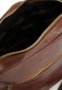 Brun læder skuldertaske med guld lynlås, der har en foret indvendig del mærket med "Venezia" og et enkelt lynlåsrum.
