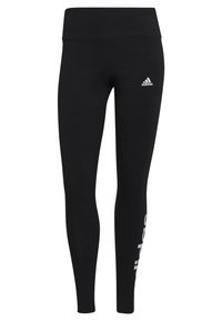 Svarta leggings i stretchmaterial med hög midja, prydda med en vit Adidas-logotyp på vänster höft och vertikal text längs benet.