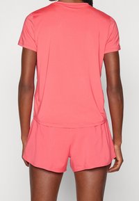 Camiseta deportiva color coral de manga corta, combinada con shorts a juego. Fabricada en tejido ligero, con un dobladillo redondeado y costuras laterales.