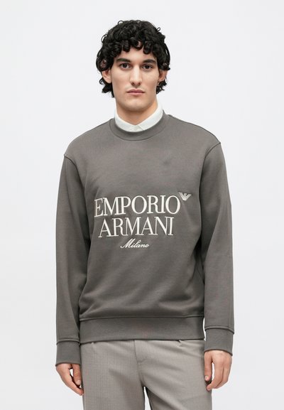Sivá bavlnená mikina s nápisom "EMPORIO ARMANI" a "Milano" v bielej farbe. Má okrúhly výstrih a rebrované manžety pre priliehavý vzhľad.