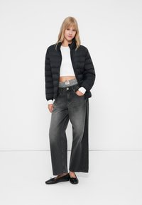 Melna pūkaina jaka ar aizdari priekšpusē, balts īss tops un platajiem pelēkajiem džinsiem ar melnbaltu rakstainu jostu. Melnas zemās kurpes.