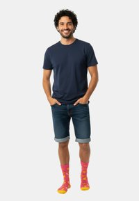 Granatowy t-shirt z krótkim rękawem, jeansowe szorty z podwiniętymi mankietami oraz jaskrawo różowe skarpetki z żółtymi wzorami bananów.