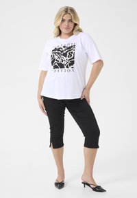 Biela T-shirt s čiernym grafickým dizajnom, v kombinácii s čiernymi skrátenými nohavicami s bočnými rozparkami. Čierne lodičky s ostrou špičkou dopĺňajú celý outfit.