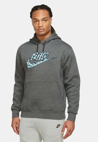 Grå hættetrøje med kengurulomme og et blåt og hvidt mønstret Nike-logo på brystet. Lavet af et blødt, tekstureret stof.