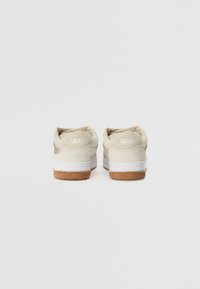Beige suede sneakers with white rubber soles and gum accents. The back features a raised logo and a padded collar for comfort.