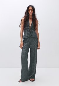 Tenue deux pièces vert foncé comprenant un haut sans manches avec un nœud à l'avant et un pantalon à jambes larges avec un motif géométrique texturé.